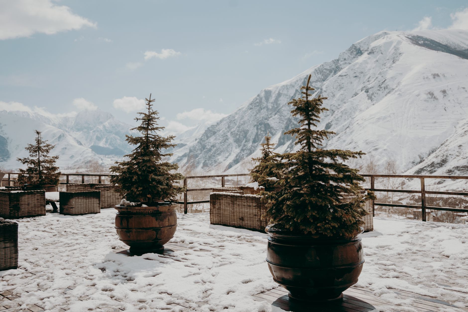 Serene snowy terrace with potted evergreens and mountain backdrop in winter.