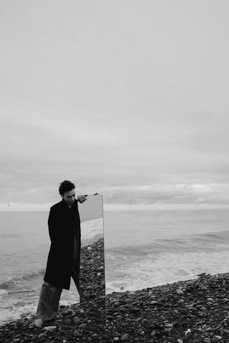 A Man Standing On The Beach While Holding A Mirror