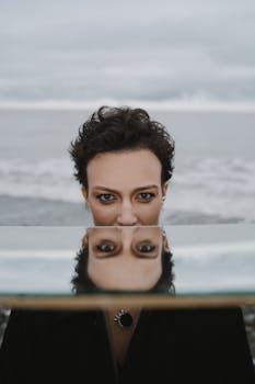 Artistic portrait of a woman with mirror reflection by the ocean, moody tone.