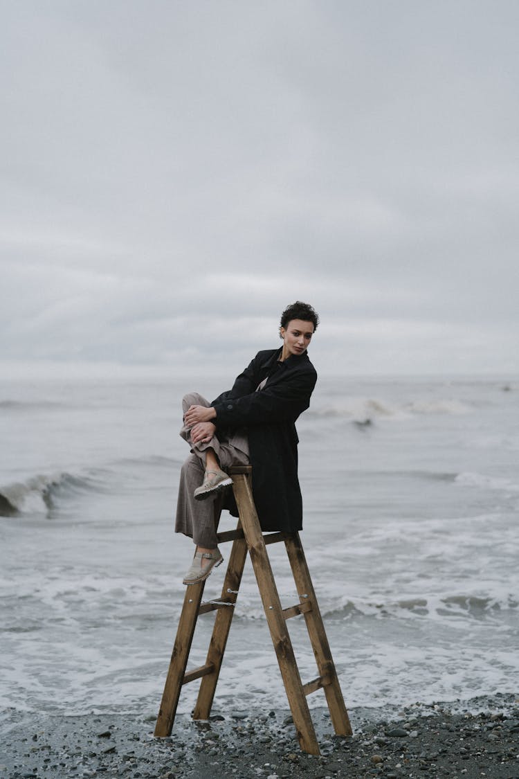 A Woman In Black Coat Sitting On Wooden Ladder