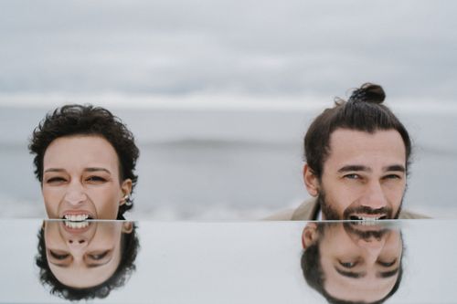 Free A creative portrait of a man and woman biting a mirror on a beach, with playful reflections. Stock Photo