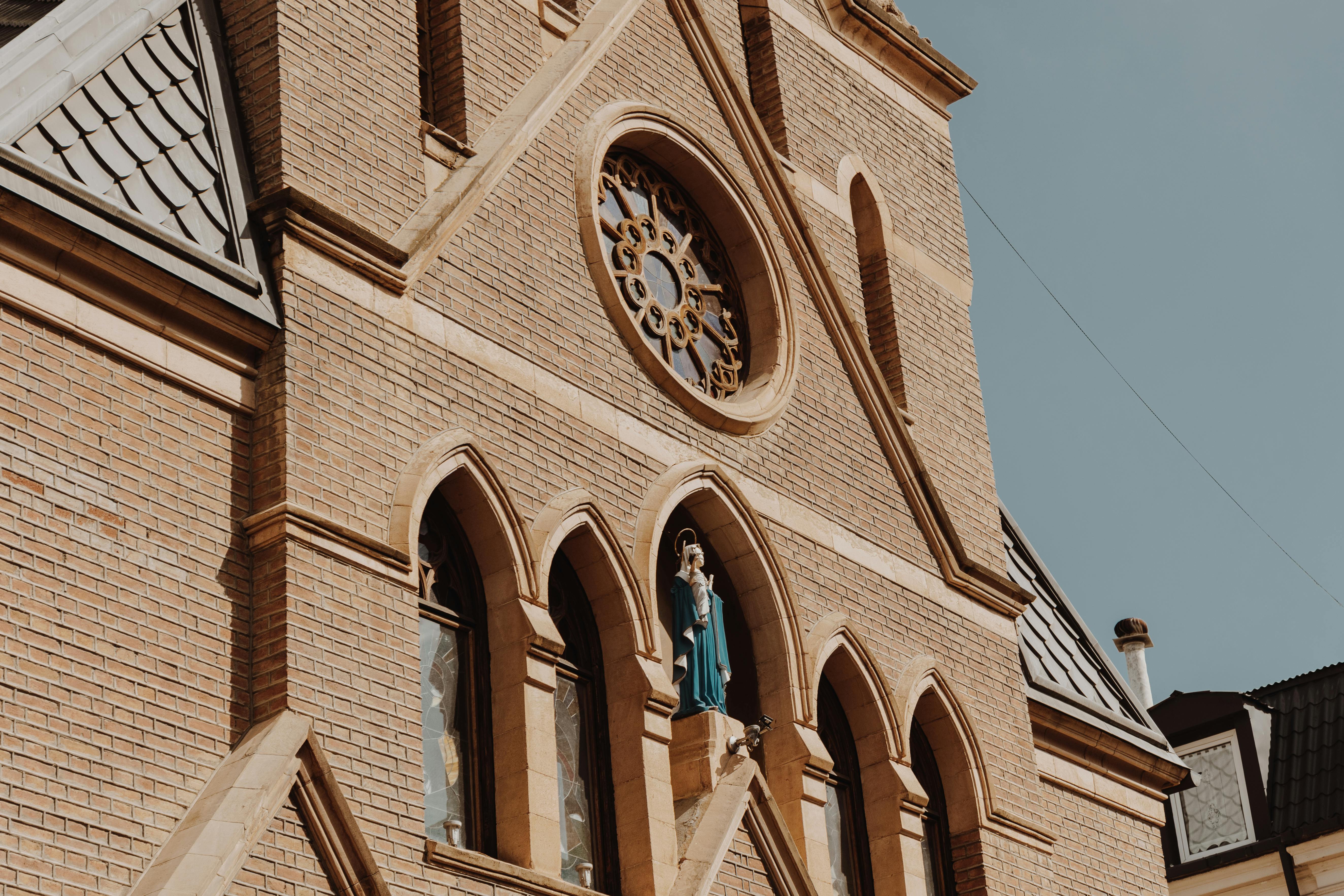 Close-up of a Gothic church facade featuring brickwork, stained glass windows, and religious statues.