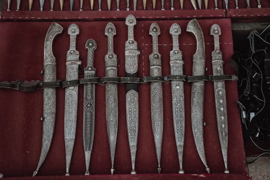 An array of intricately designed antique daggers with ornate handles on a red display surface.