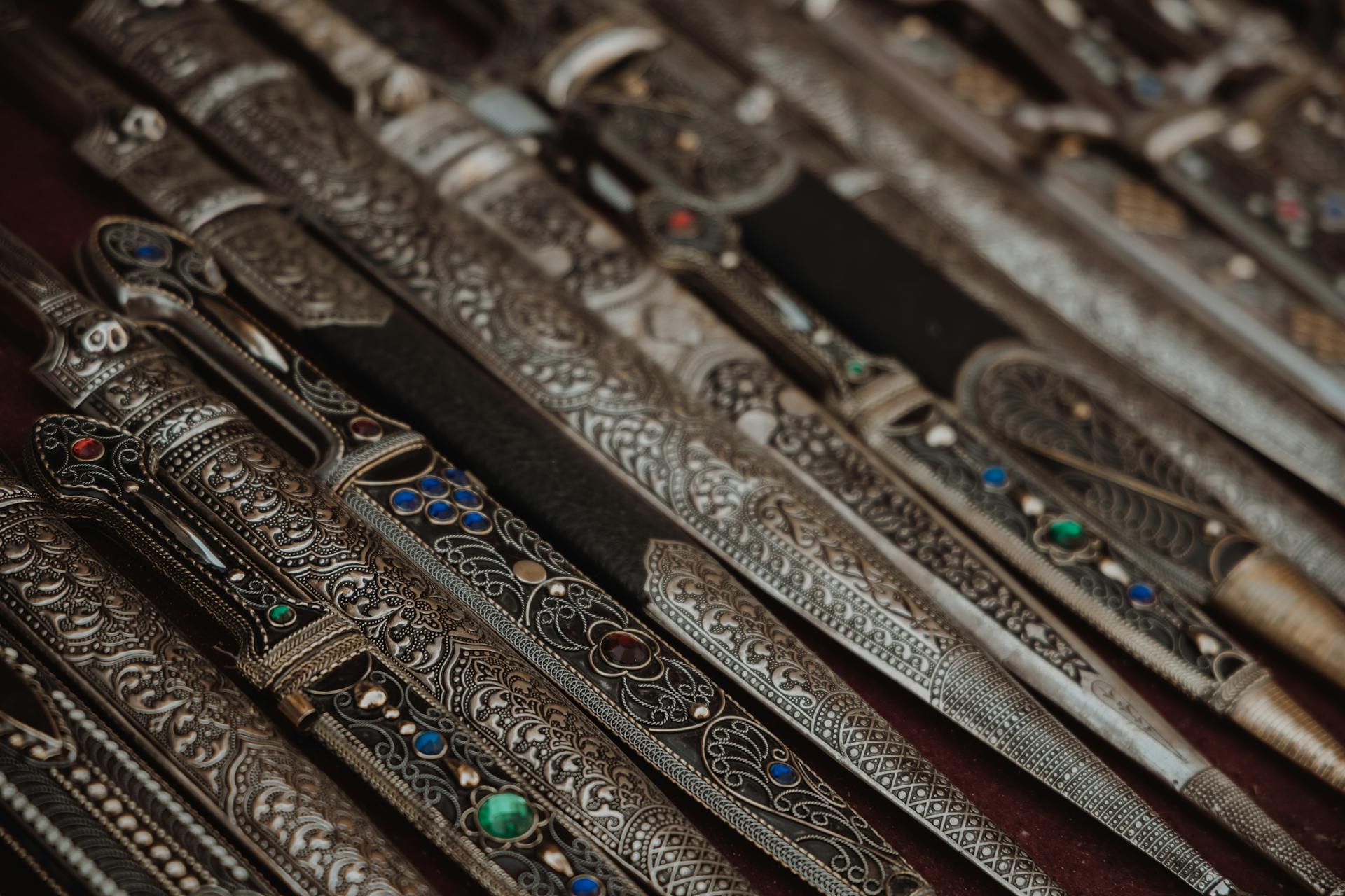 Close-up of several ornate daggers with detailed engravings and colored jewel inlays.