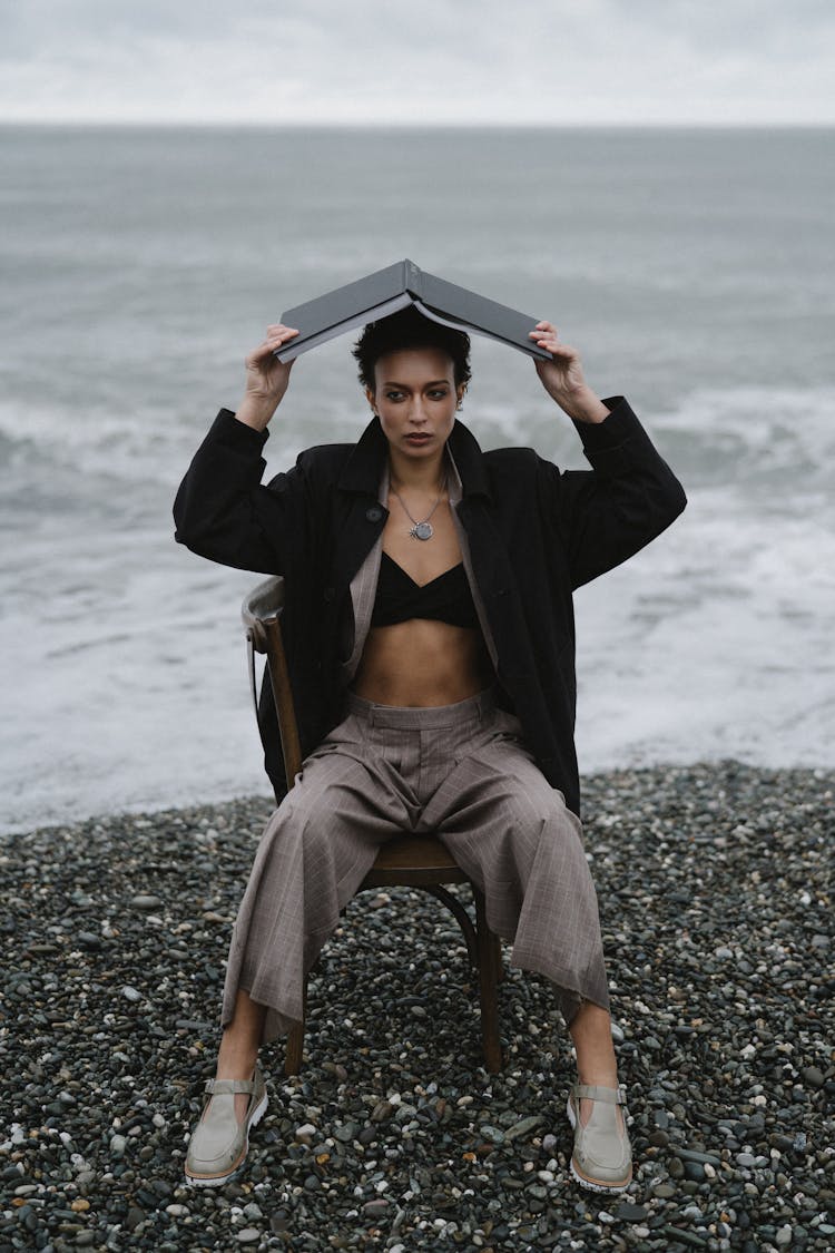 A Woman In Black Coat Covering Her Head With A Book