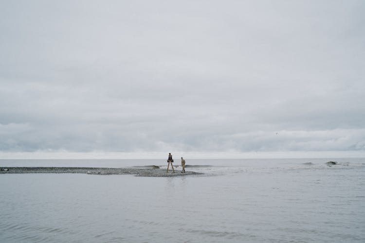 People Sitting On A Ladder And Standing On A Sandbar Of A Sea