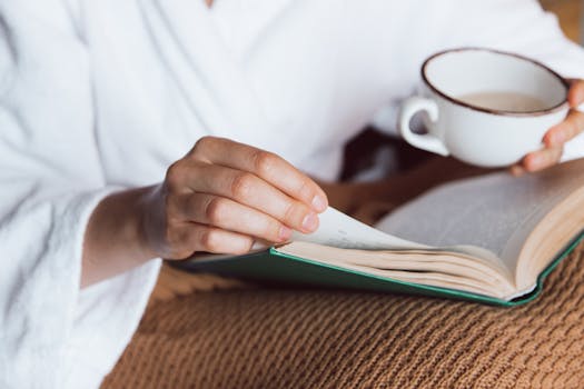 A person enjoys a peaceful morning with a book and a cup of coffee, wrapped in a cozy robe.