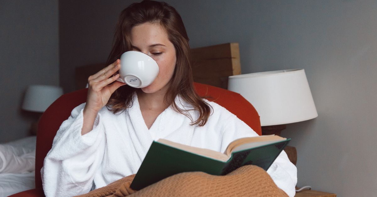 person reading a book in a cozy chair with a cup of tea, looking thoughtful