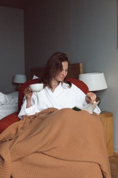 Woman in bathrobe enjoys reading with a cup of coffee in a cozy indoor setting, enhancing relaxation.