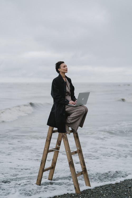 Free A Woman Sitting on a Ladder While using Laptop Stock Photo