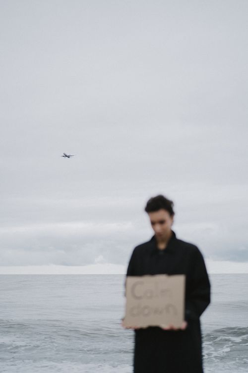 Free Blurry figure holding sign by the sea with a plane overhead. Stock Photo
