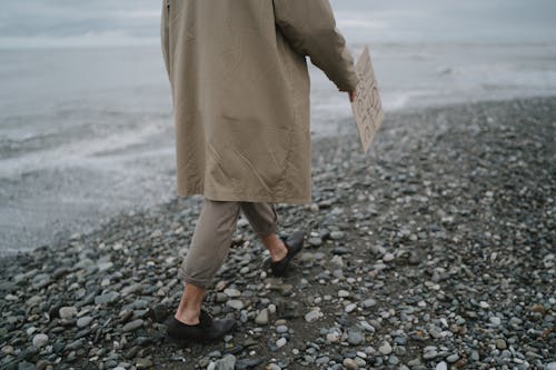 Free A Person in Brown Coat Walking on a Rocky Shore Stock Photo