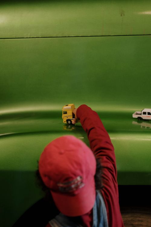 Free A child in a red cap plays with toy trucks on a vibrant green surface in a workshop setting. Stock Photo