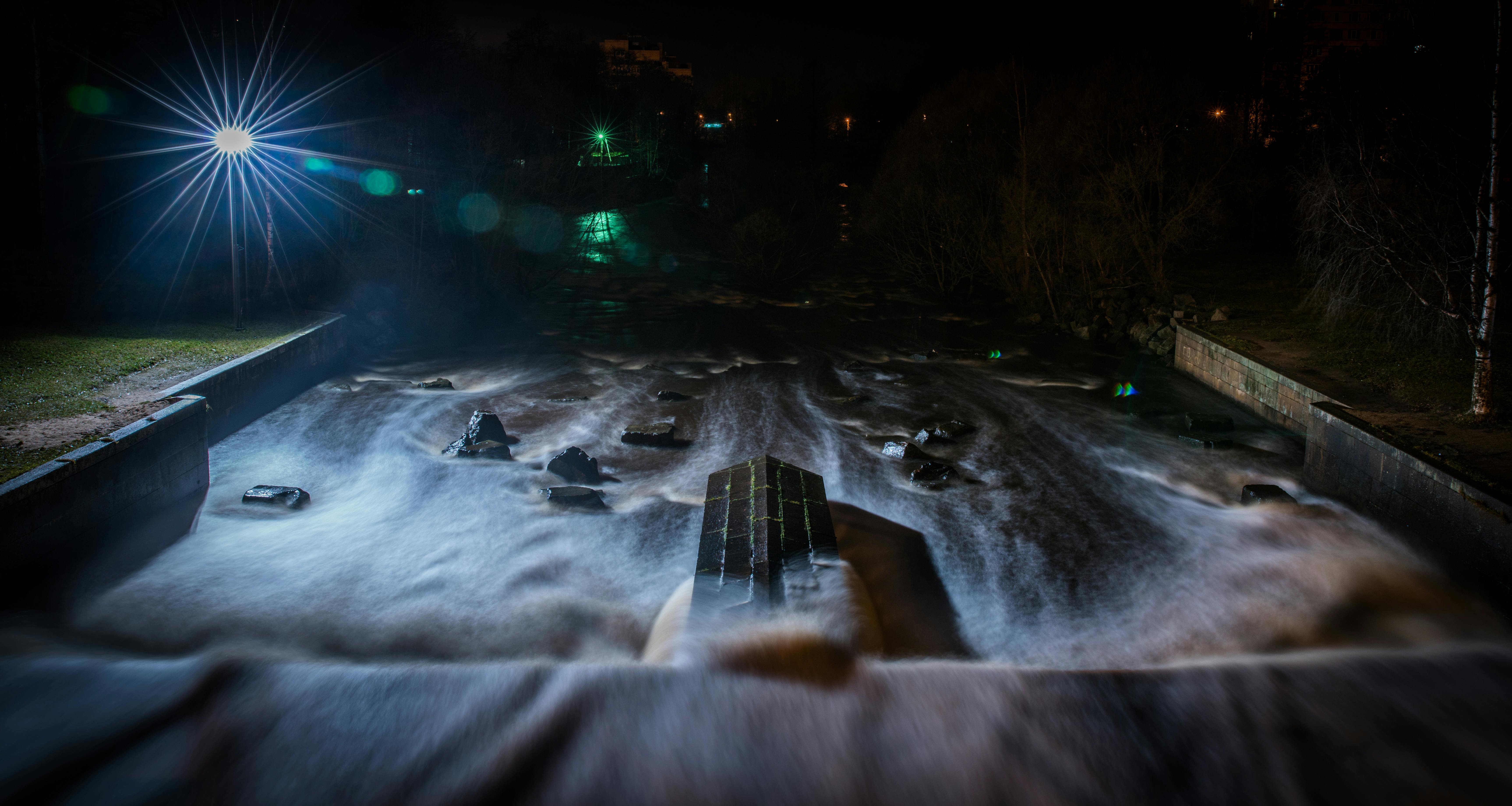 这是一张长曝光照片，捕捉了夜间河流的活力景象，水面上映着引人注目的光线反射，水流间弥漫着薄雾