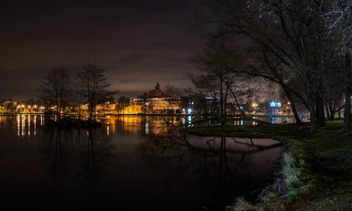 Still Body of Water Next to Lighted Beige Buildings during Nighttime