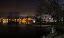 夜晚，一个宁静的城市天际线倒映在平静的湖面上，灯光闪烁，树木成剪影