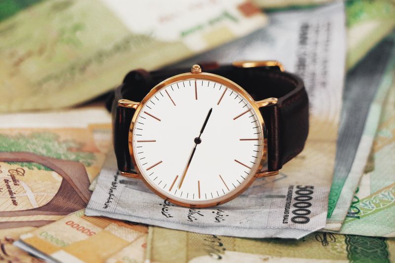 A sophisticated wristwatch resting atop Iranian rial notes, symbolizing time's value in Tehran.