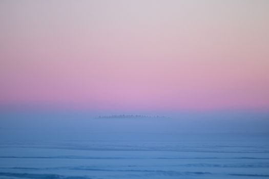 Tranquil scene of ocean enveloped in mist with a pink and blue sunset sky.