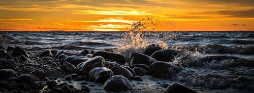 免费 日落期间在海滩上的石头溅起的海浪 素材图片