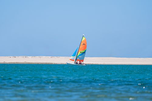 Free A vibrant sailboat sails on the clear blue waters against a sandy backdrop in Dubai. Stock Photo