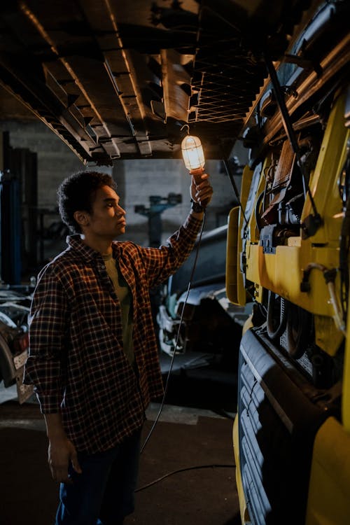 A Man Looking under the Hood of a Truck with a Garage Work Light