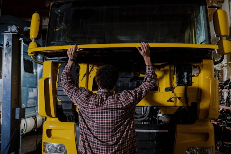 A Person Looking Under The Hood Of A Truck