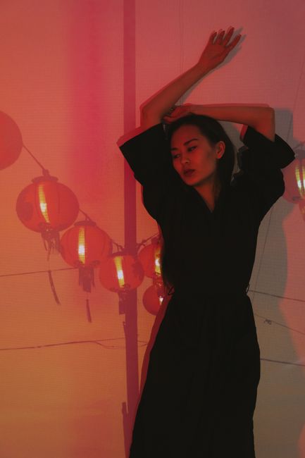 A woman poses gracefully indoors with vibrant Chinese lanterns casting warm light.