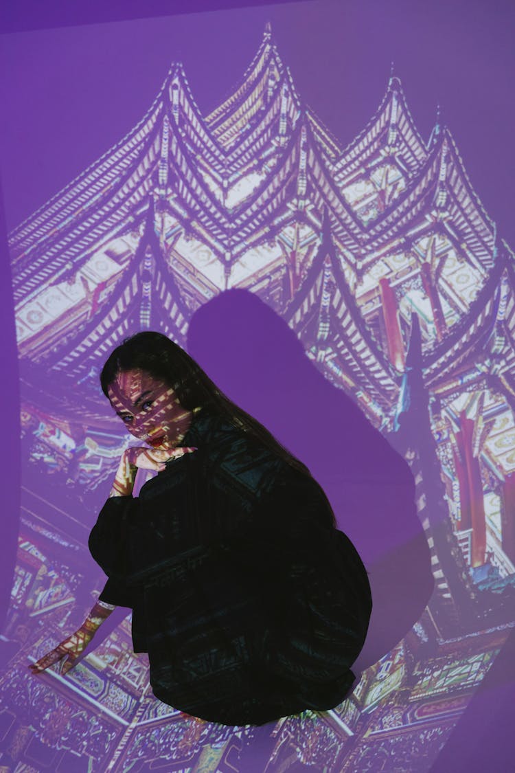 A Woman Wearing Black Robe Sitting In Front Of The Projector Light Showing A Pagoda Roof