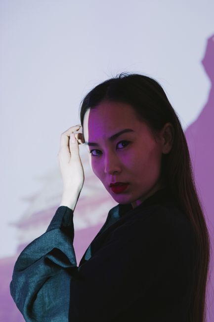 Stylish portrait of an Asian woman with dramatic lighting casting shadows indoors.