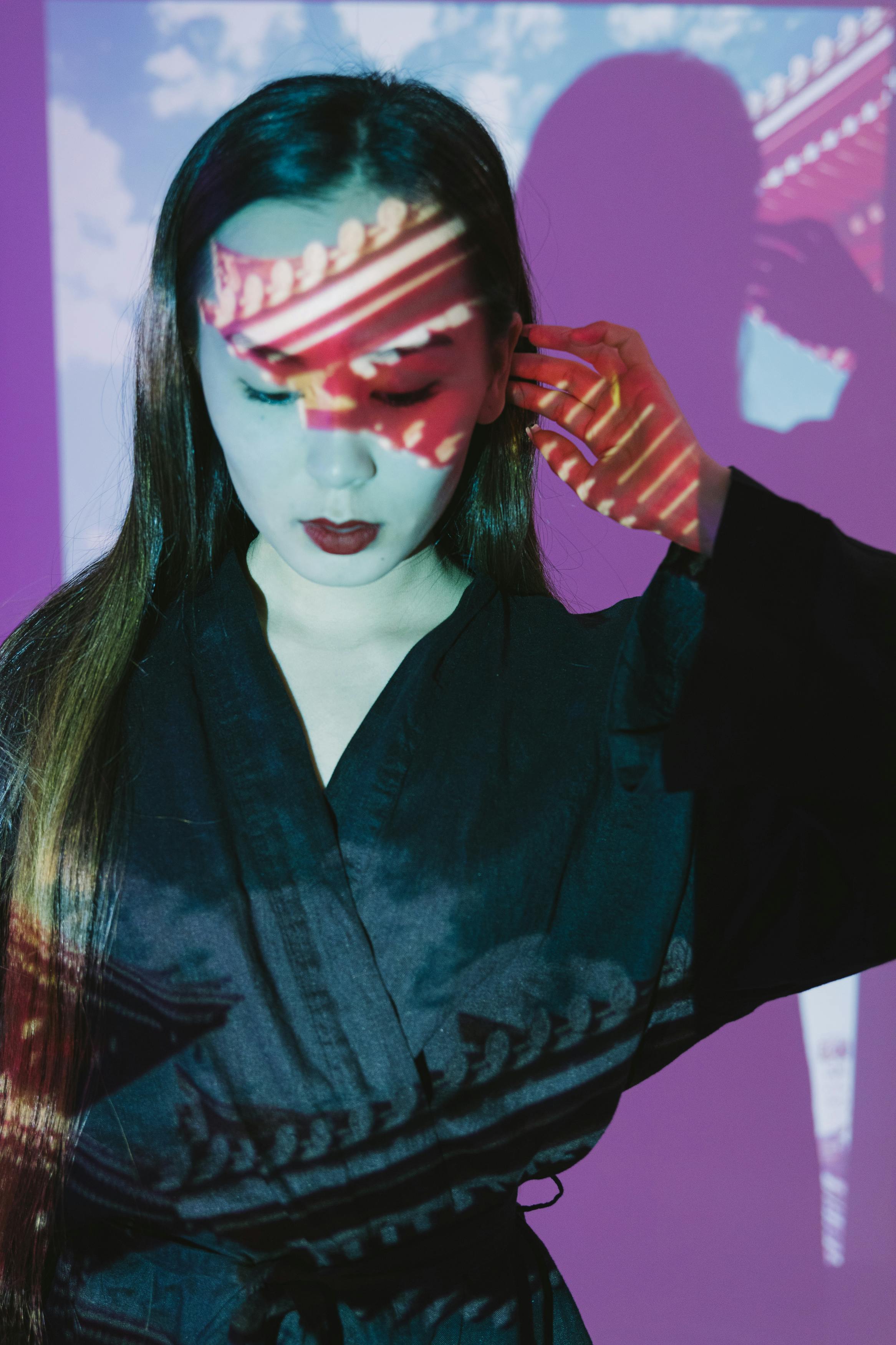 Elegant portrait of an Asian woman with colorful projections on her face in a black dress.