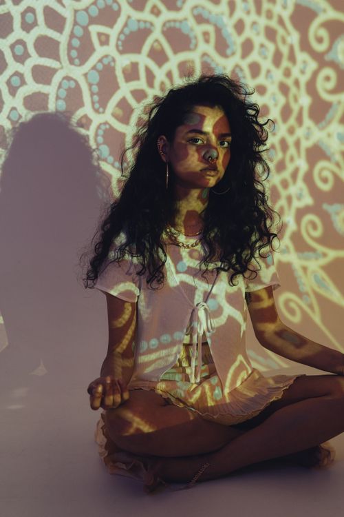 Free Woman meditating with intricate patterned light projection, creating a serene and artistic atmosphere. Stock Photo