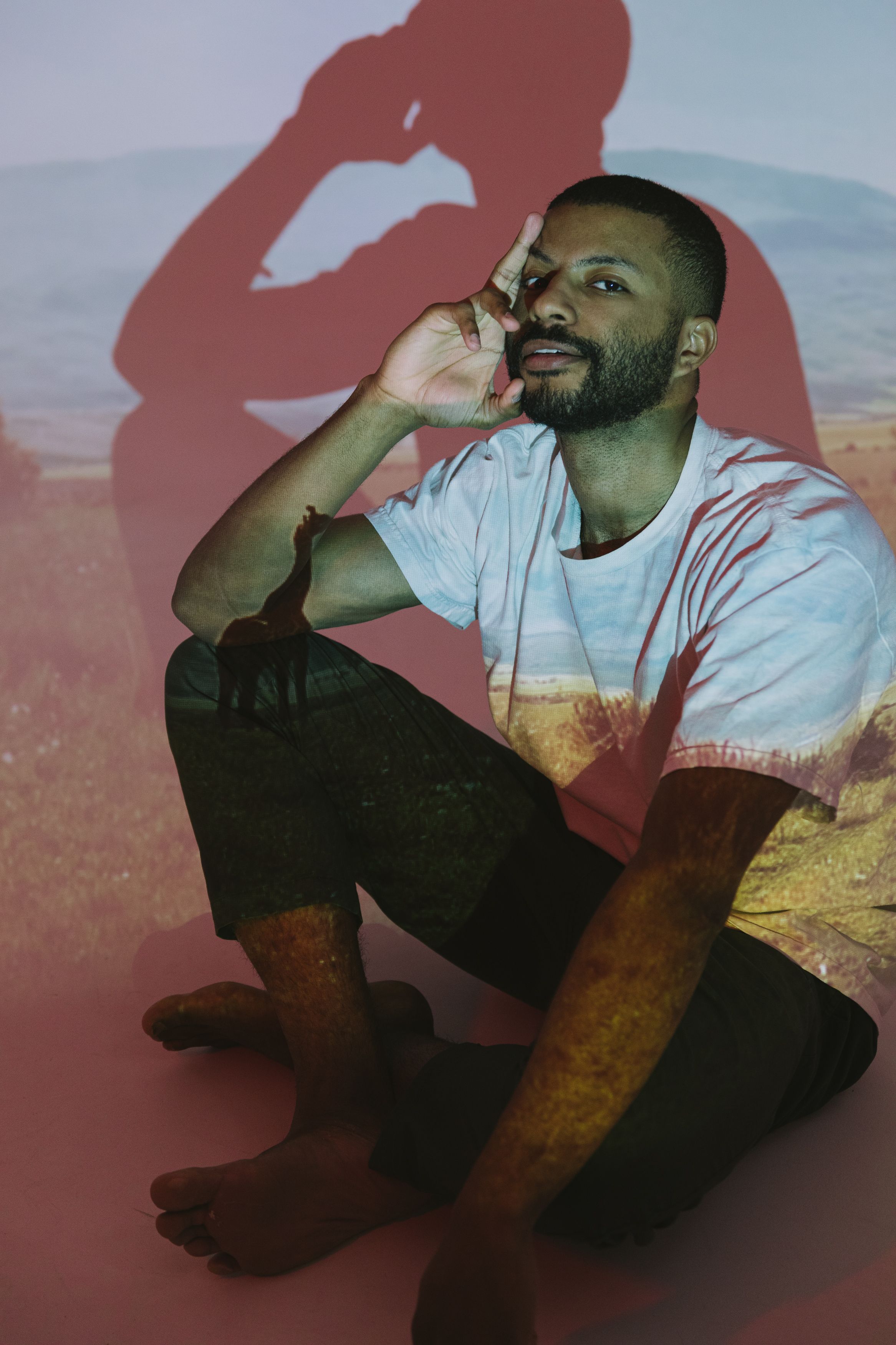 Artistic portrait of a man seated with projected imagery on his body in a contemplative pose.