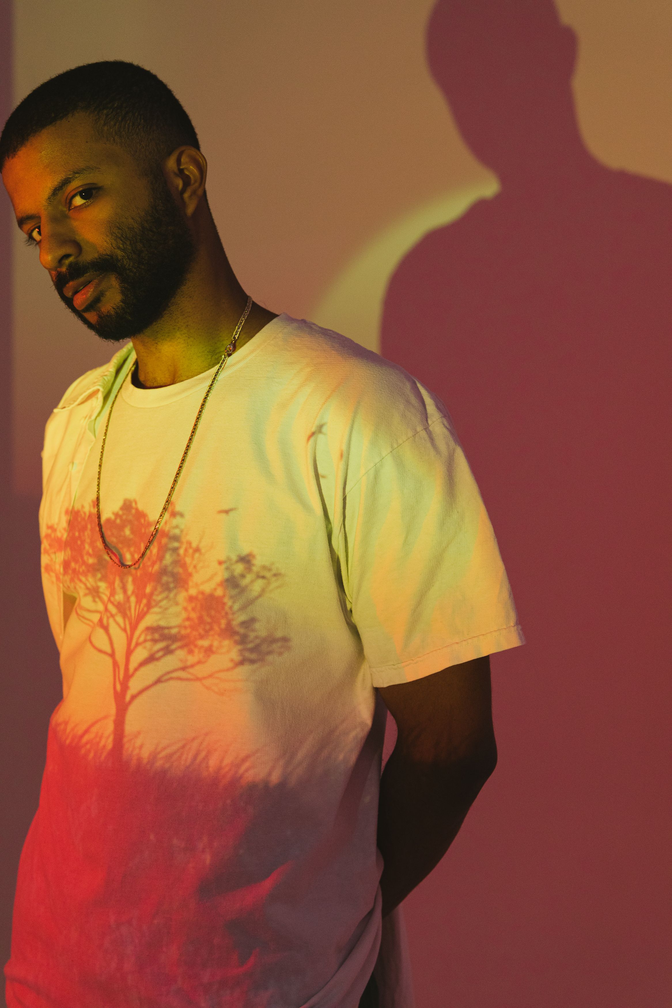 Fashionable man poses in colorful studio lighting with creative shadows.