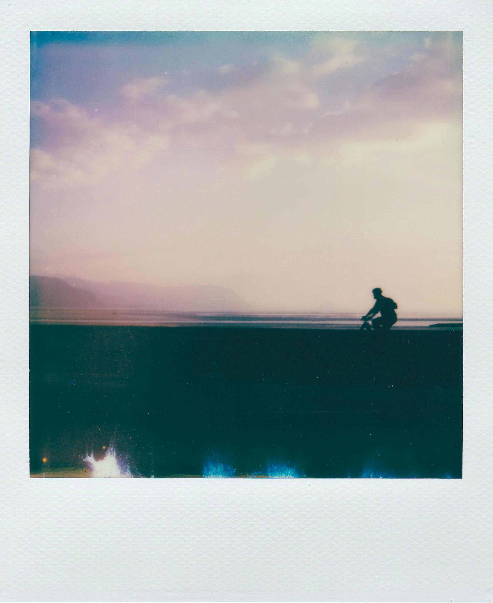 Vintage-style silhouette of a cyclist at twilight with serene sky and coastline.