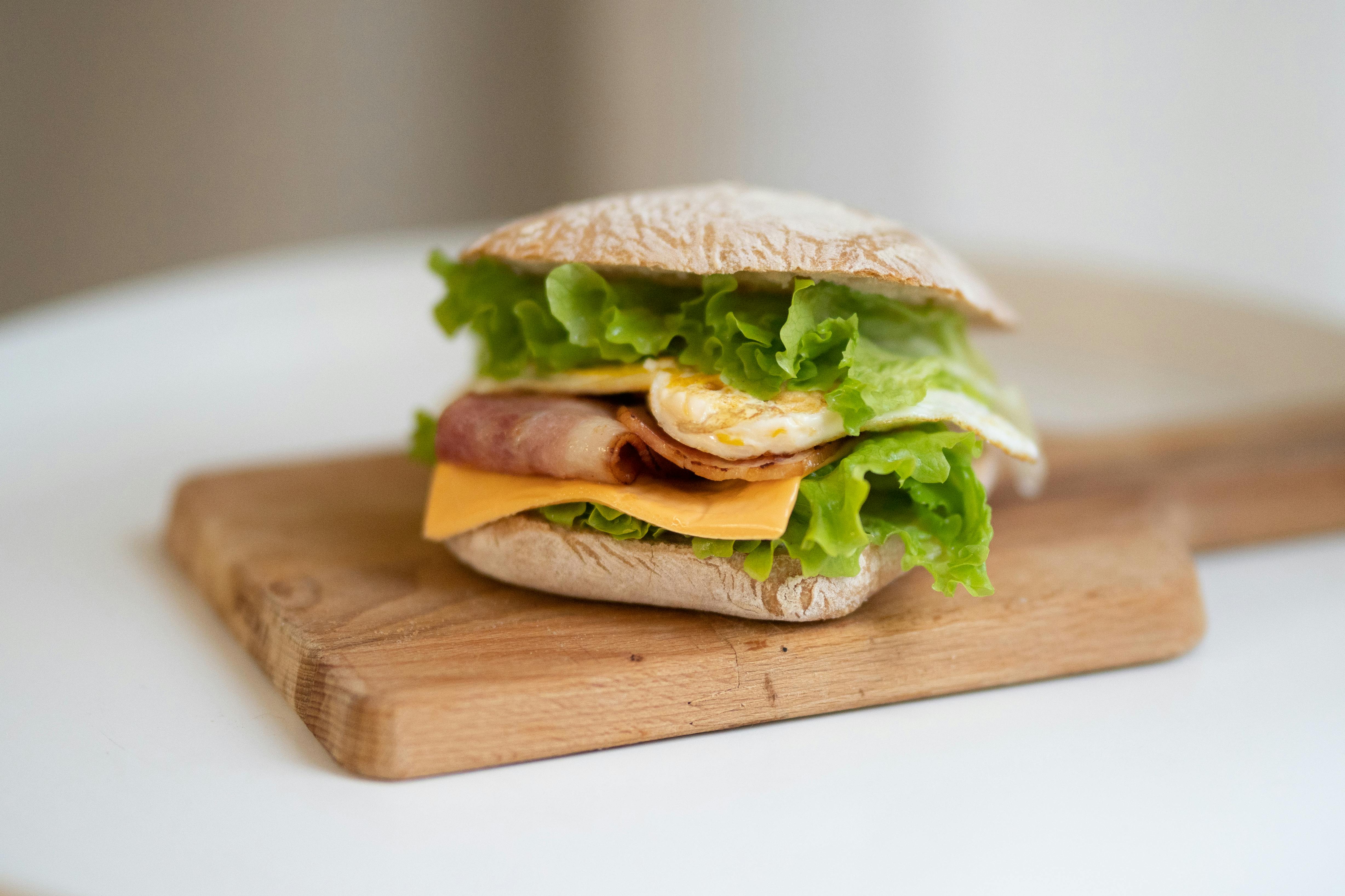 Free Delicious sandwich with bacon, lettuce, cheese, and egg on a wooden board. Stock Photo