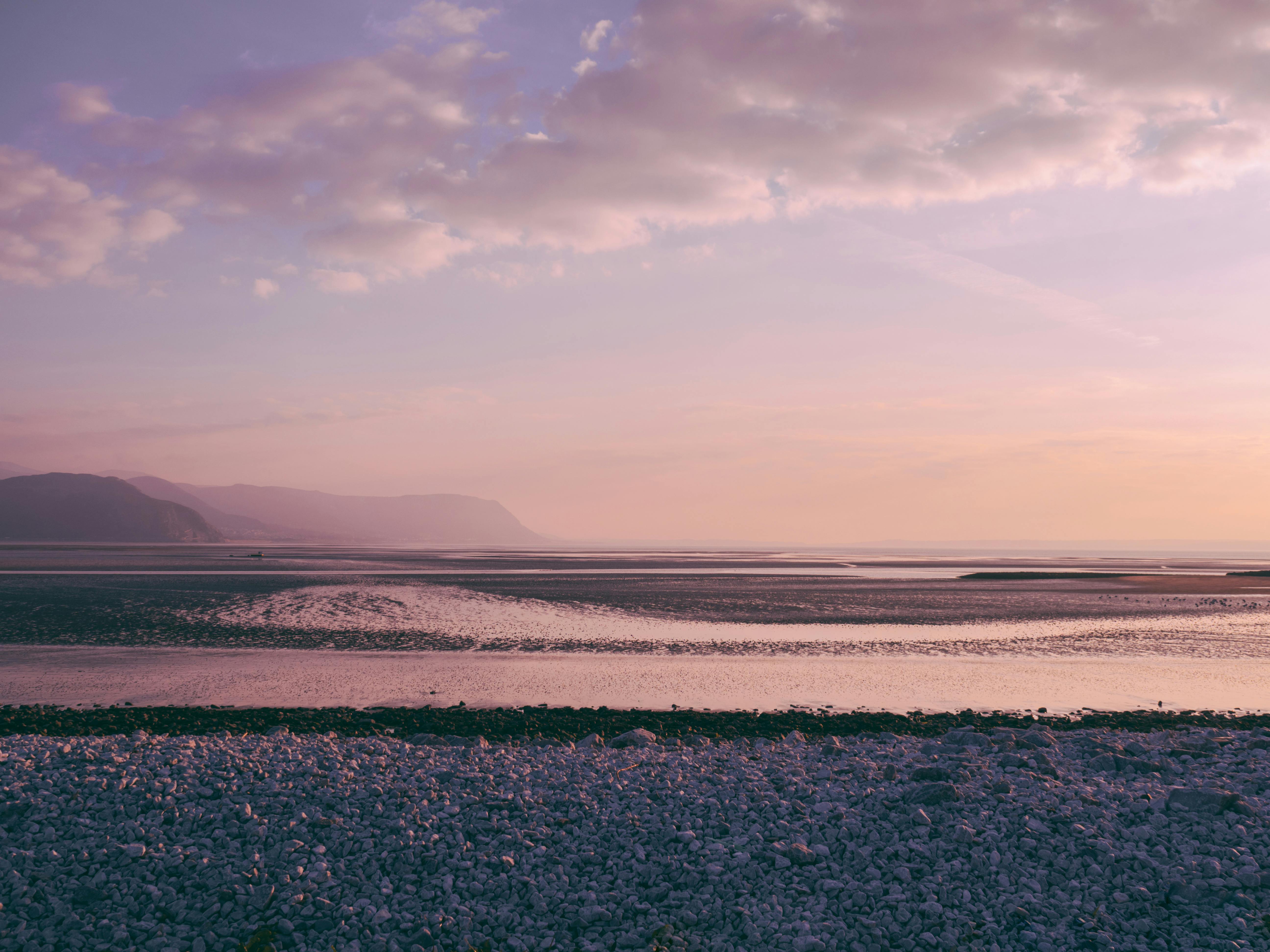 Peaceful view of Llandudno's rocky shore at sunset with distant mountains in Wales.