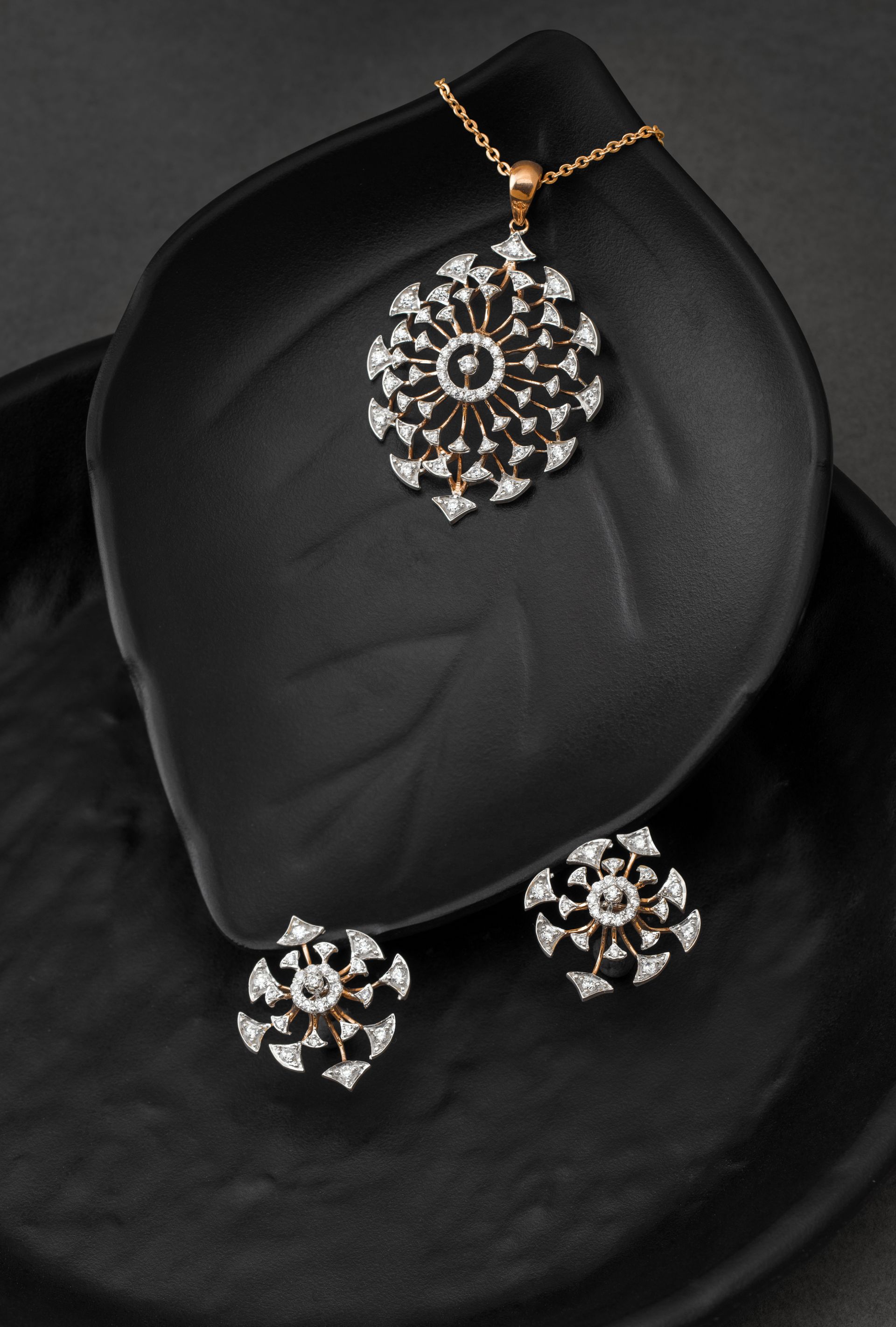 Luxurious gold and diamond jewelry set featuring a pendant and earrings on a black leaf-shaped surface