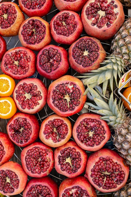 From above of fresh appetizing pomegranates with pineapples and oranges arranged on metal tray in market