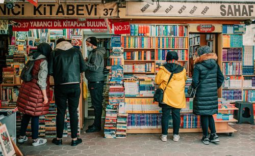 Free Back view of anonymous people in outerwear standing near bookshelves and choosing books on street Stock Photo