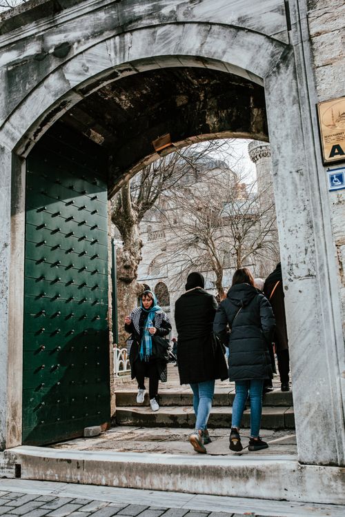 Free Visitors in warm clothes walking through arched gates into yard of mosque in daytime Stock Photo