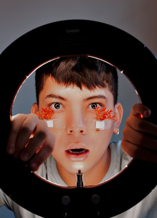 Amazed ethnic man with flowers on face against ring light