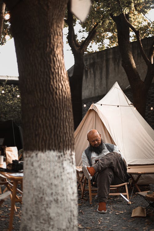 Man in Gray Jacket Sitting on Brown Wooden Chair Near White Tent