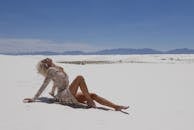 蔚蓝天空下，一名身着闪亮连衣裙的女子在广阔的白色沙漠中优雅地摆出姿势