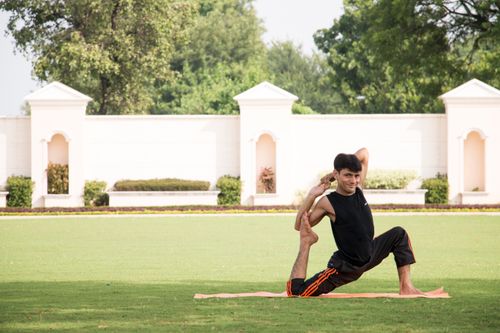 Free Man performing yoga pose on mat in a sunny park. Healthy lifestyle and wellness concept. Stock Photo