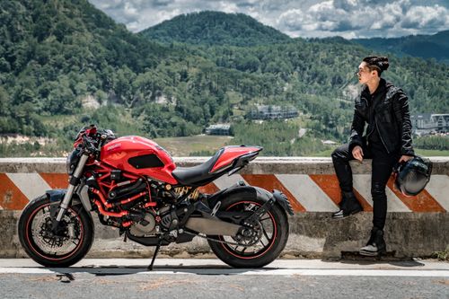 Free Man sitting on roadside barrier, enjoying scenic mountain view with red motorcycle. Stock Photo