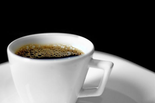 A close-up view of a ceramic coffee cup filled with espresso, isolated on a black background.