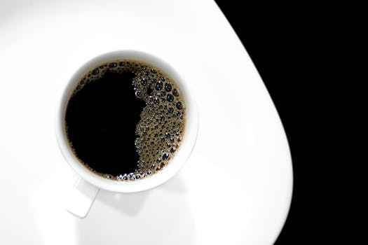An artistic top view of black coffee in a white ceramic cup on a contrasting black background.