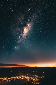 A stunning view of the Milky Way galaxy over a lit New Zealand town under a starry night sky.