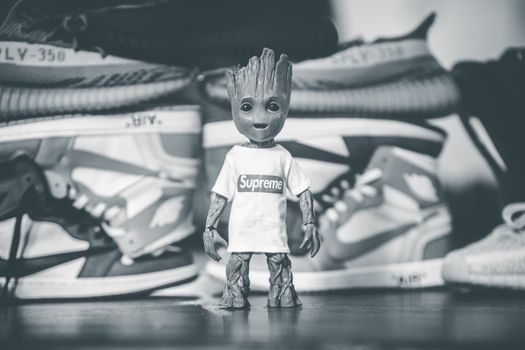 A trendy toy figurine wearing a Supreme shirt stands in front of sneakers, offering a modern streetwear vibe.