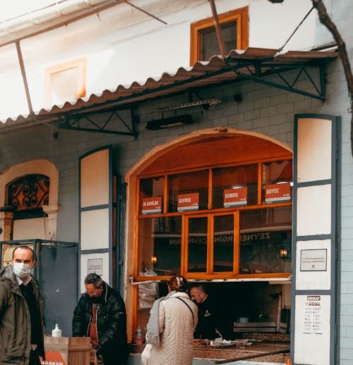 Woman consulting with seller in mask working in cafe offering traditional takeaway food on street